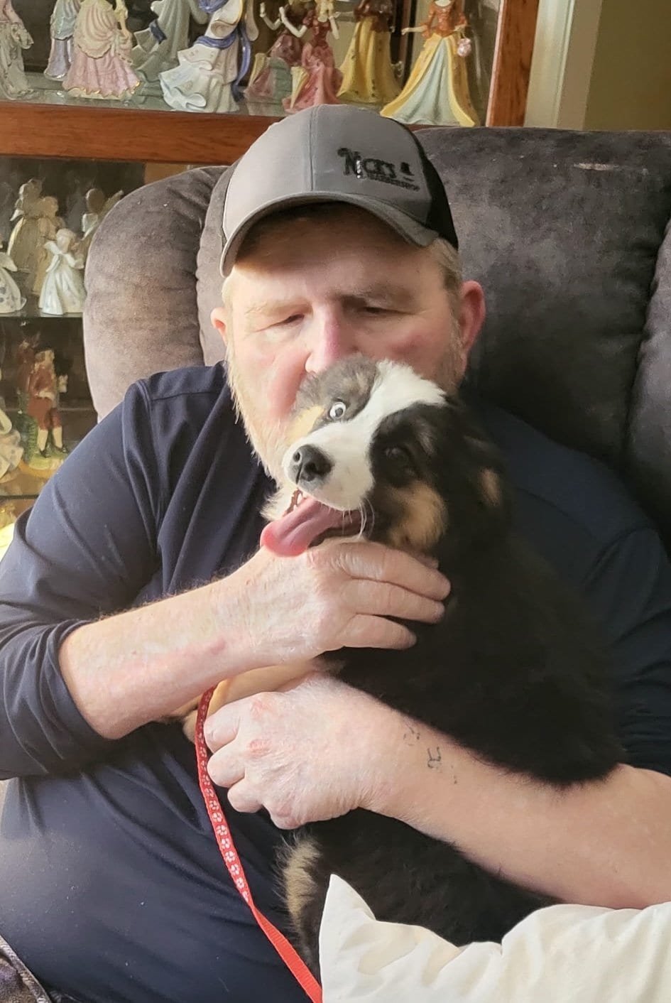 Man holding a happy puppy, sitting on a sofa, in a cozy home setting.