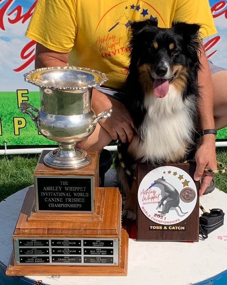 Dog holding trophy and award at the Ashley Wippet Invitational World Canine Frisbee Championships.