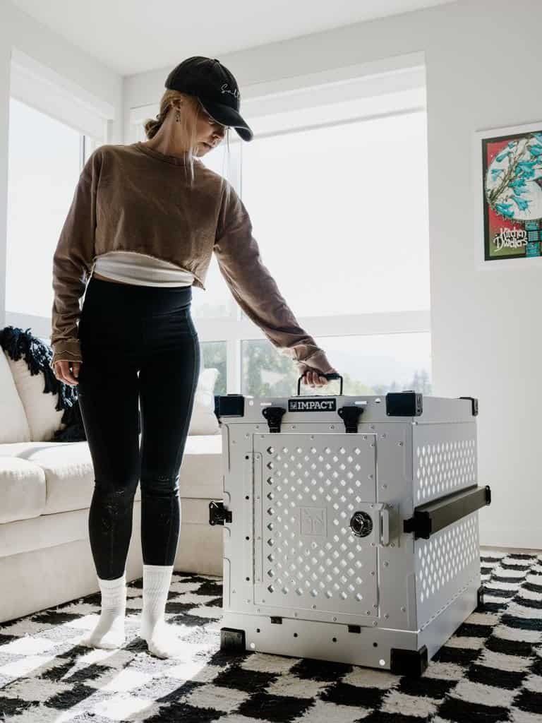 A woman stands beside a high-quality dog crate in a stylish indoor setting.